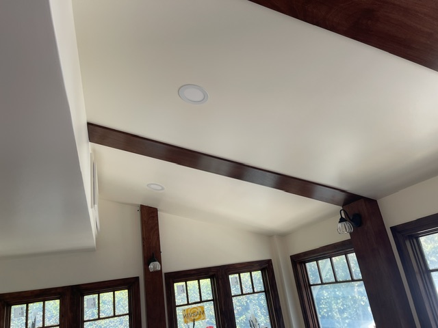 Ceiling with recessed lighting, exposed dark wood beams, and large windows allowing natural light into the room.